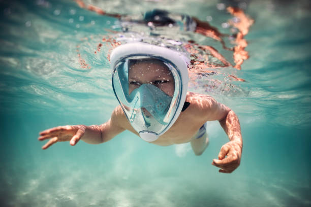 Happy little boy swimming underwater, wearing a modern full-face snorkel mask.